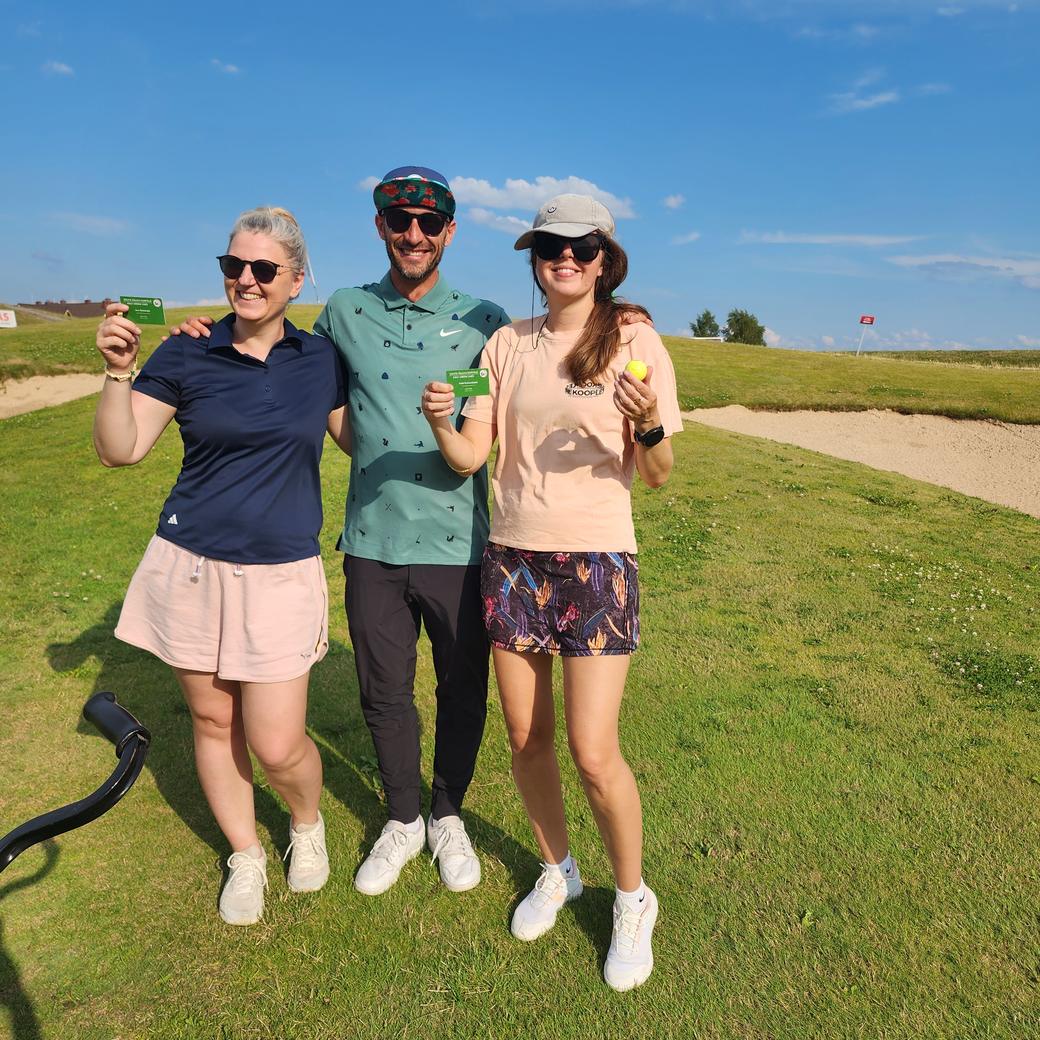 Three golfers on a Lithuanian course holding up their new golf green cards, coach Donatas in the centre.